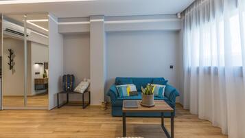 A modern living room with a blue sofa, a coffee table with a laptop, a plant, and a mirror reflecting the room.