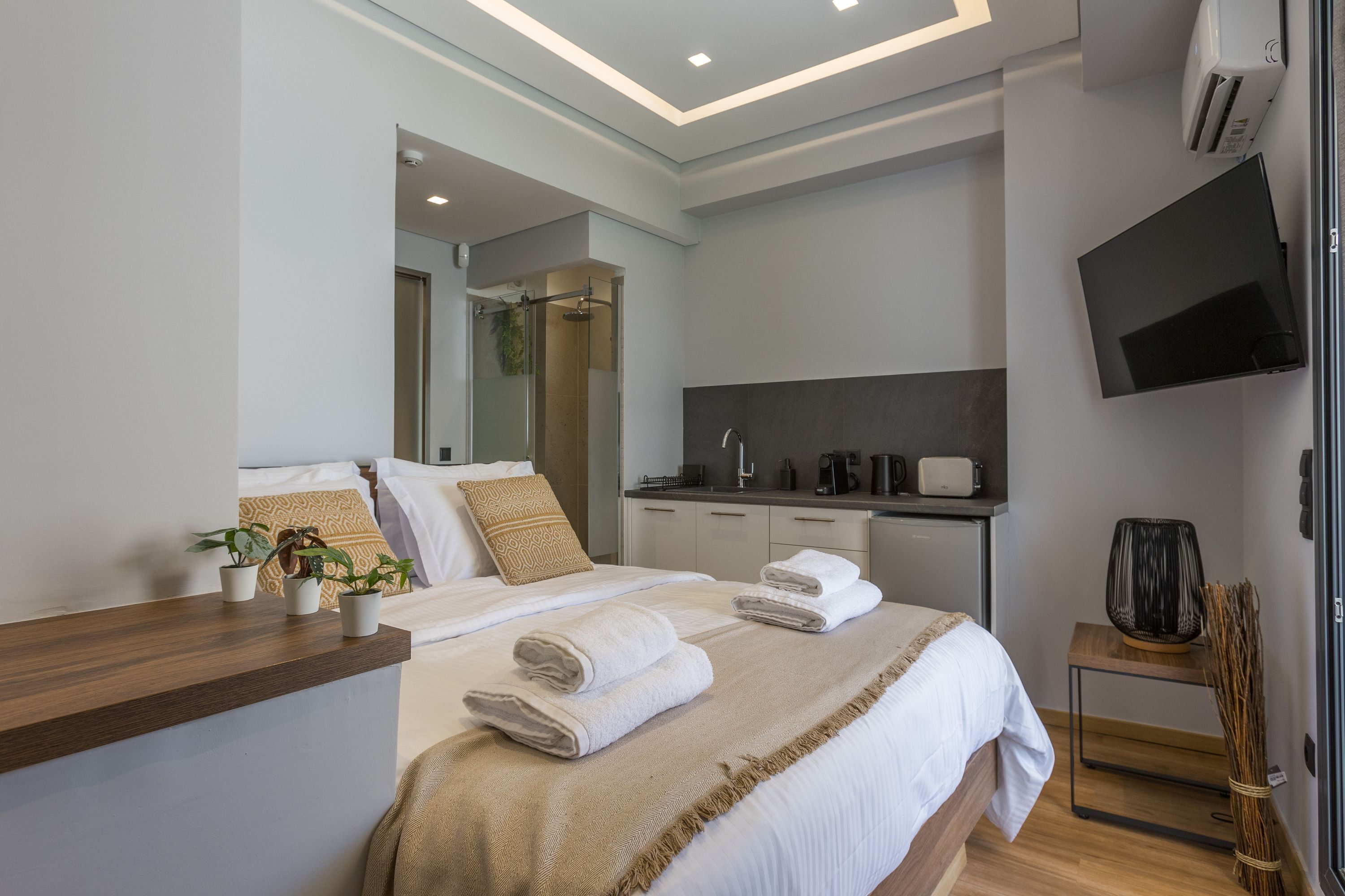 Une chambre d’hôtel moderne dotée d’un grand lit, d’une table de chevet en bois, d’un téléviseur à écran plat, d’un petit coin cuisine et d’une douche.