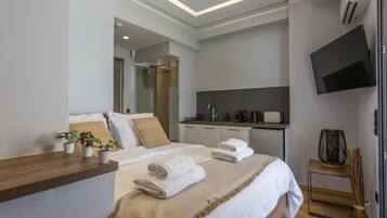 Une chambre d’hôtel moderne dotée d’un grand lit, d’une table de chevet en bois, d’un téléviseur à écran plat, d’un petit coin cuisine et d’une douche.