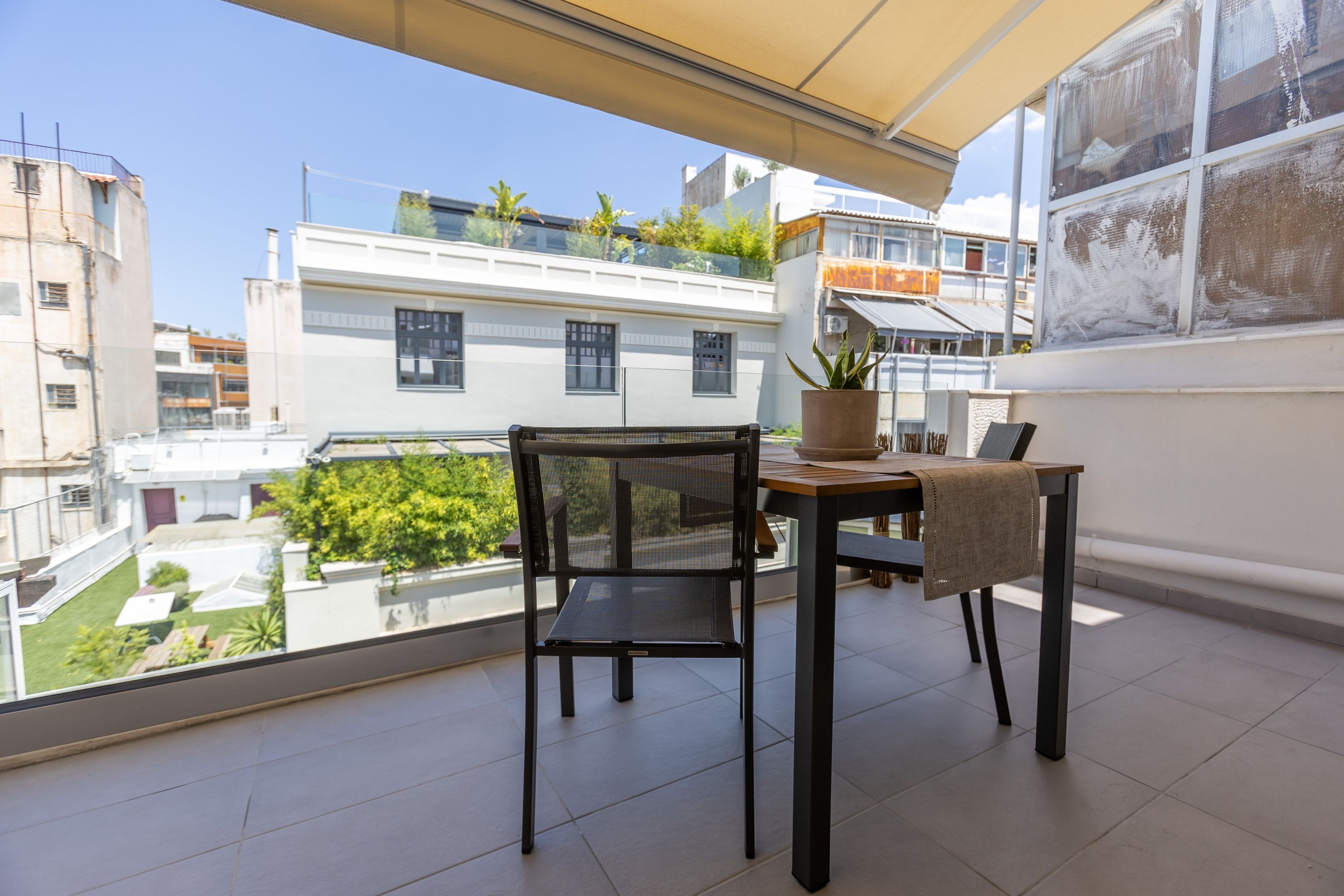 Un balcon avec une table et une chaise, un pot de fleurs et une vue sur le paysage urbain.