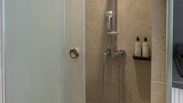 Une douche fermée par des parois en verre, dotée d’un pommeau de douche à main, d’un robinet mural et d’une petite étagère pour les articles de toilette.