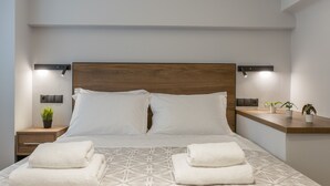 Ein ordentlich bezogenes Bett mit einem geometrisch gemusterten Überwurf, zwei Nachttische mit Lampen und eine kleine Ablage mit Topfpflanzen.