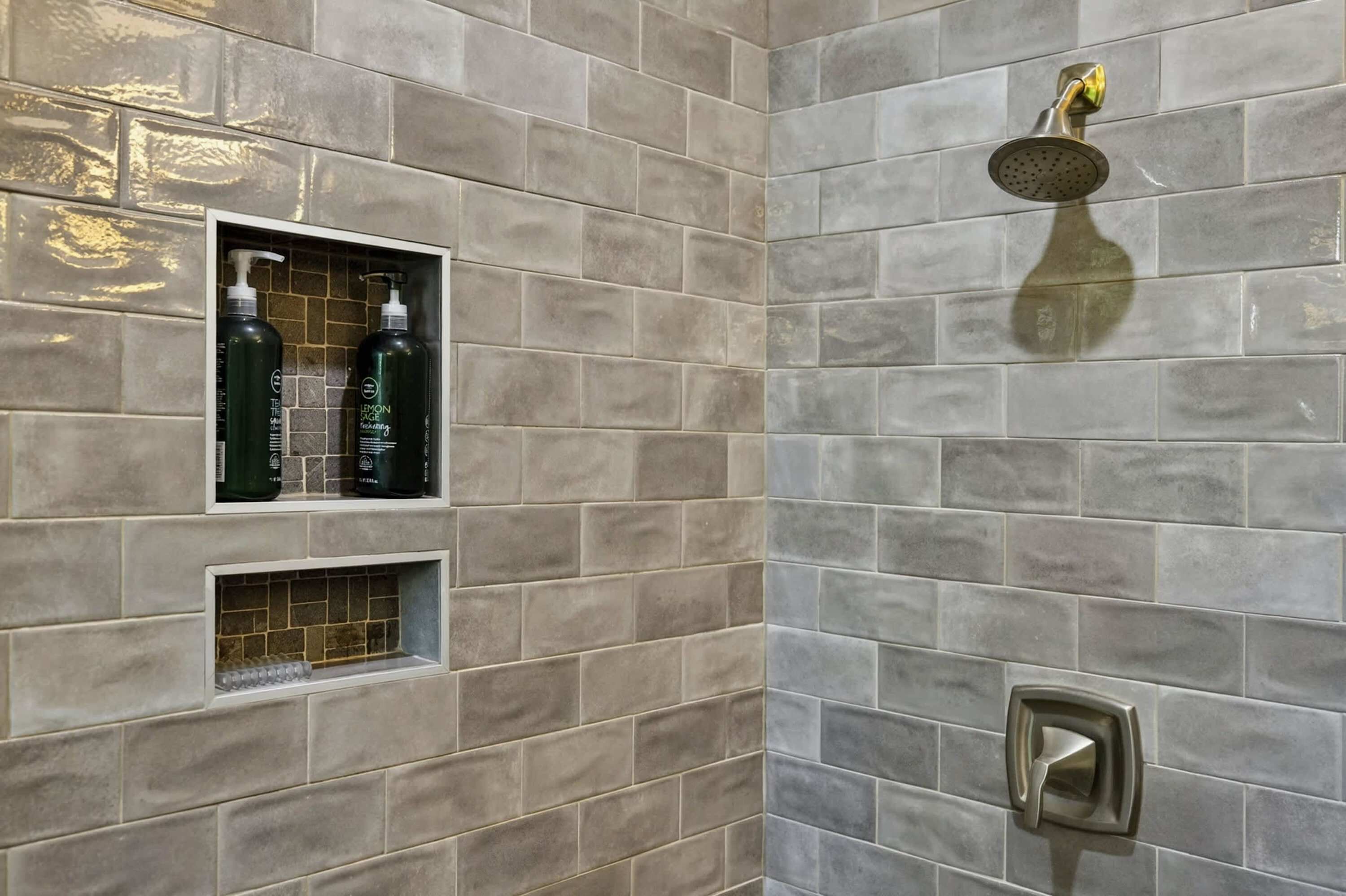 A shower area with a handheld showerhead, a soap dispenser, and a glass shelf.