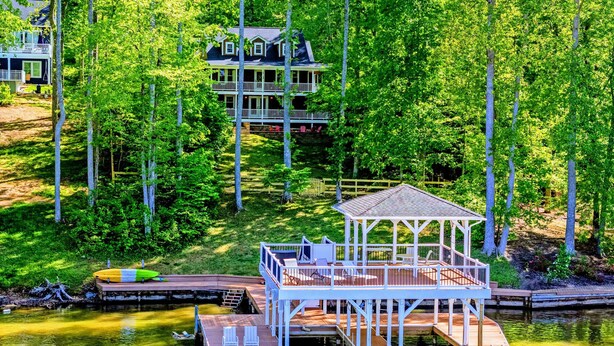 Una proprietà sul lago con un pontile, un gazebo e una casa a più piani immersa tra gli alberi.