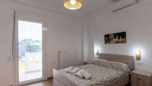 Un dormitori amb un llit, una taula de nit, una làmpada penjada a la paret, un radiador i una porta corredissa de vidre a un balcó.