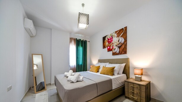 Una habitación de hotel con cama, mesita de noche, lámpara y una obra de arte en la pared.