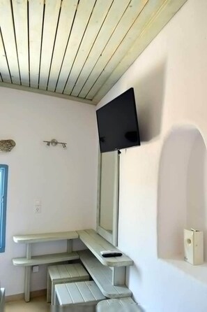 Quarto com teto inclinado, televisão de tela plana na parede, um banco e uma pequena mesa.