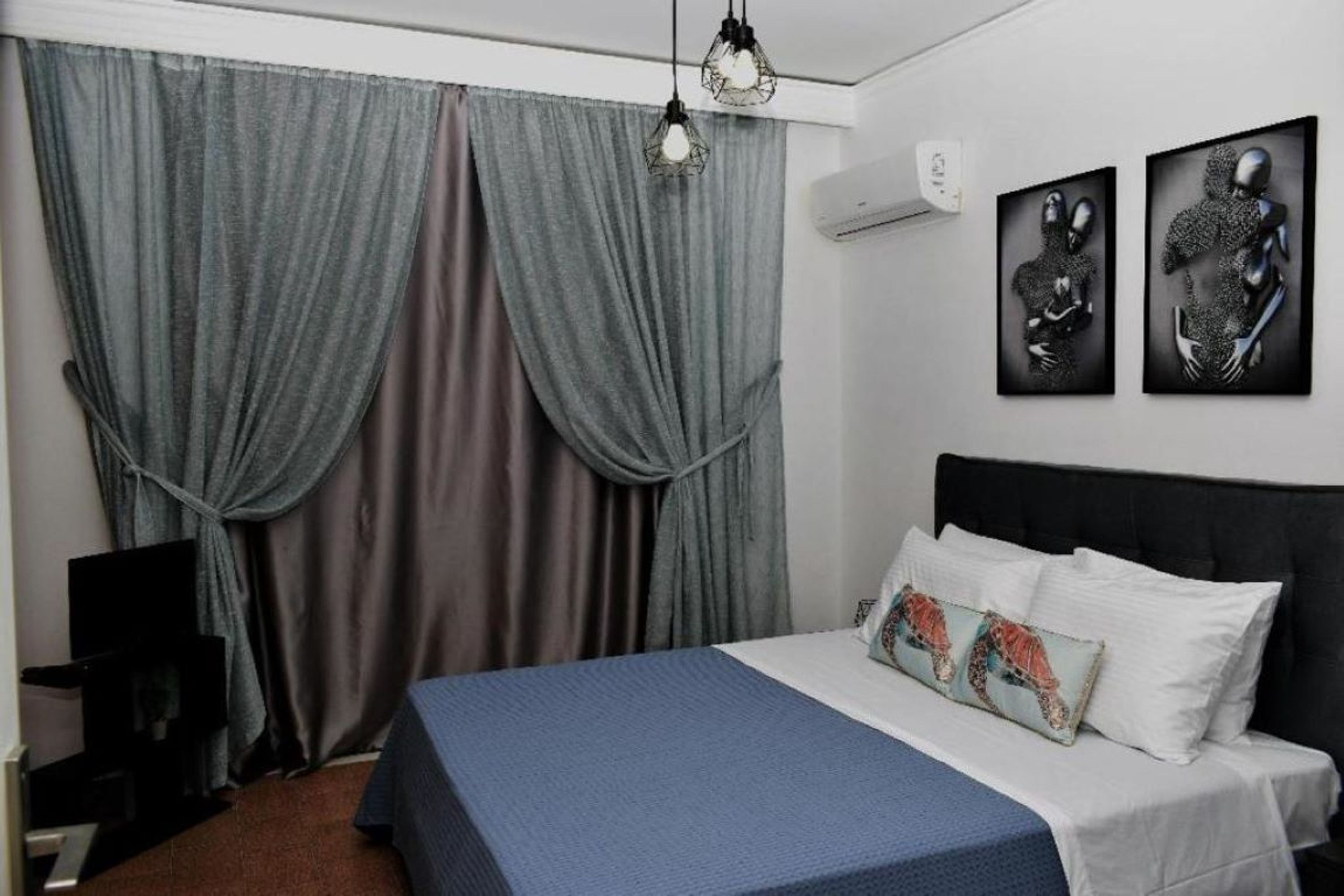 Une chambre à coucher avec un lit, des rideaux, des œuvres d’art murales et un appareil de climatisation.