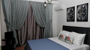 Une chambre à coucher avec un lit, des rideaux, des œuvres d’art murales et un appareil de climatisation.