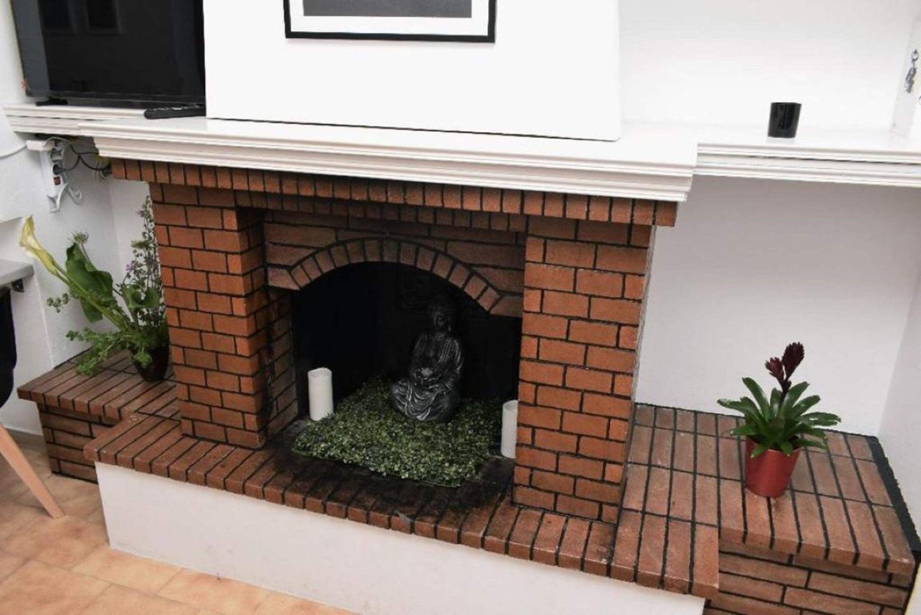 Une cheminée en briques ornée d’une statue, d’une plante en pot et d’un mur blanc.