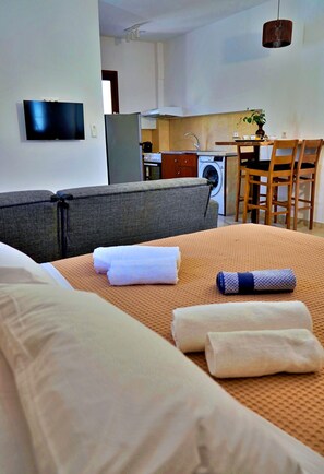 Ein Hotelzimmer mit Bett, einer Couch, einem Esstisch mit Stühlen, einer Küchenzeile und einem an der Wand befestigten Fernseher.