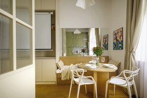 Ein moderner Essbereich mit einem Holztisch, weißen Stühlen, einer Bank und Blick in die Küche.