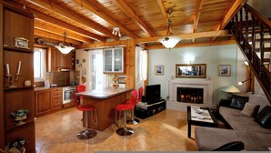 A spacious kitchen with wooden beams, a dining area with red bar stools, a living room with a fireplace, and a staircase. - Villa AnnaMaria with Swimming Pool (Heraklion)