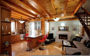A spacious kitchen with wooden beams, a dining area with red bar stools, a living room with a fireplace, and a staircase.