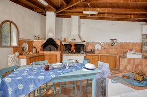 A rustic kitchen with a wood-burning stove, a dining table set for four, and a tiled backsplash.