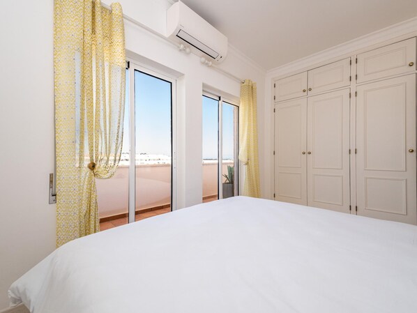 Ein Schlafzimmer mit einem großen Bett, einer Schiebetür zu einem Balkon und einem weißen Kleiderschrank.