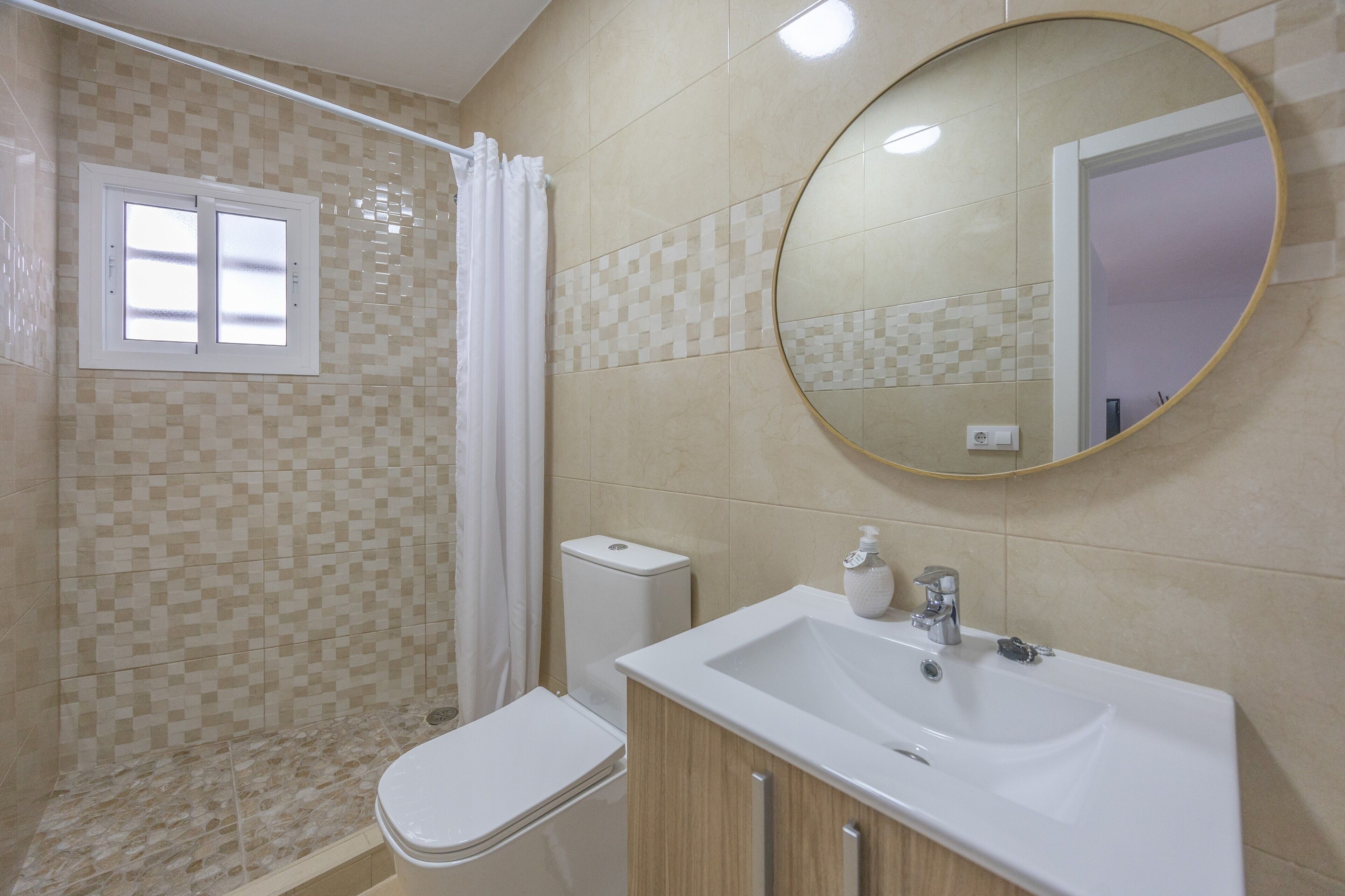 Un baño con inodoro, ducha, lavamanos y espejo.