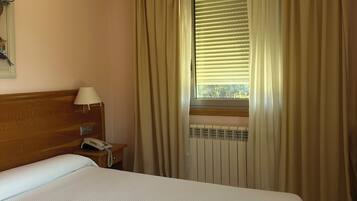 A hotel room with a bed, a nightstand with a lamp, a telephone, and a window with curtains.