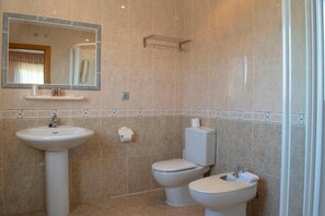 A bathroom with a pedestal sink, two toilets, a mirror, and a towel rack.