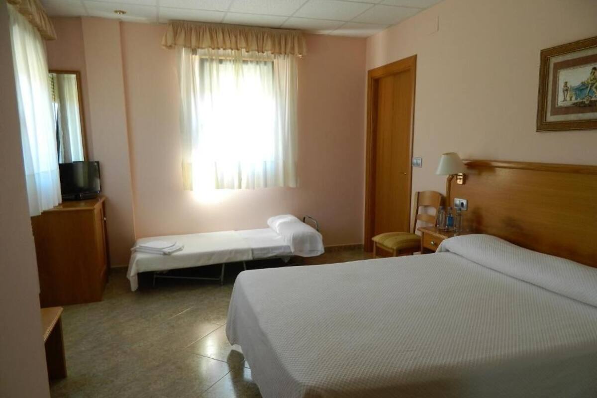 A hotel room with two beds, a television, a window with curtains, a door, and a lamp.