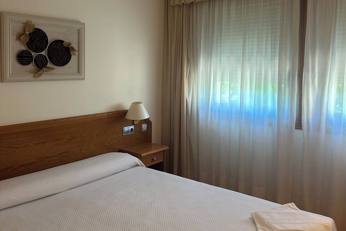 A hotel room with a bed, a nightstand with a lamp, a wall decoration, and a window with curtains.