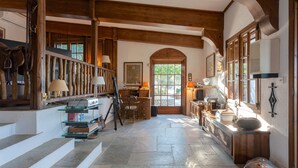 Ein rustikales Interieur mit Steinböden, Holzbalken, einer Treppe und einem Schreibtisch mit Büchern und einer Lampe.