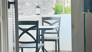 Eine offene Tür, die auf einen Balkon mit Tisch und Stühlen, einer Laterne sowie einer Aussicht auf Grünflächen und ein Gebäude im Hintergrund führt.