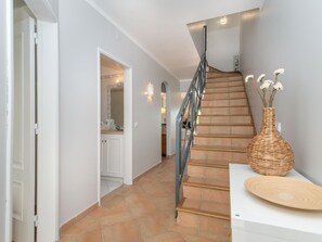 A staircase with a handrail, a white door leading to a bathroom, and a wicker vase on a white table.