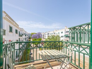 A balcony with a green metal railing, a wooden bench, and a view of white buildings with green shutters. - CB LAG 10 2.E in Conceição de Tavira (Conceição de Tavira)
