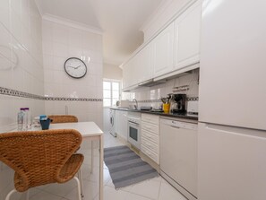 A kitchen with white cabinets, a clock, a dining table with chairs, and a coffee maker. - CB LAG 10 2.E in Conceição de Tavira (Conceição de Tavira)