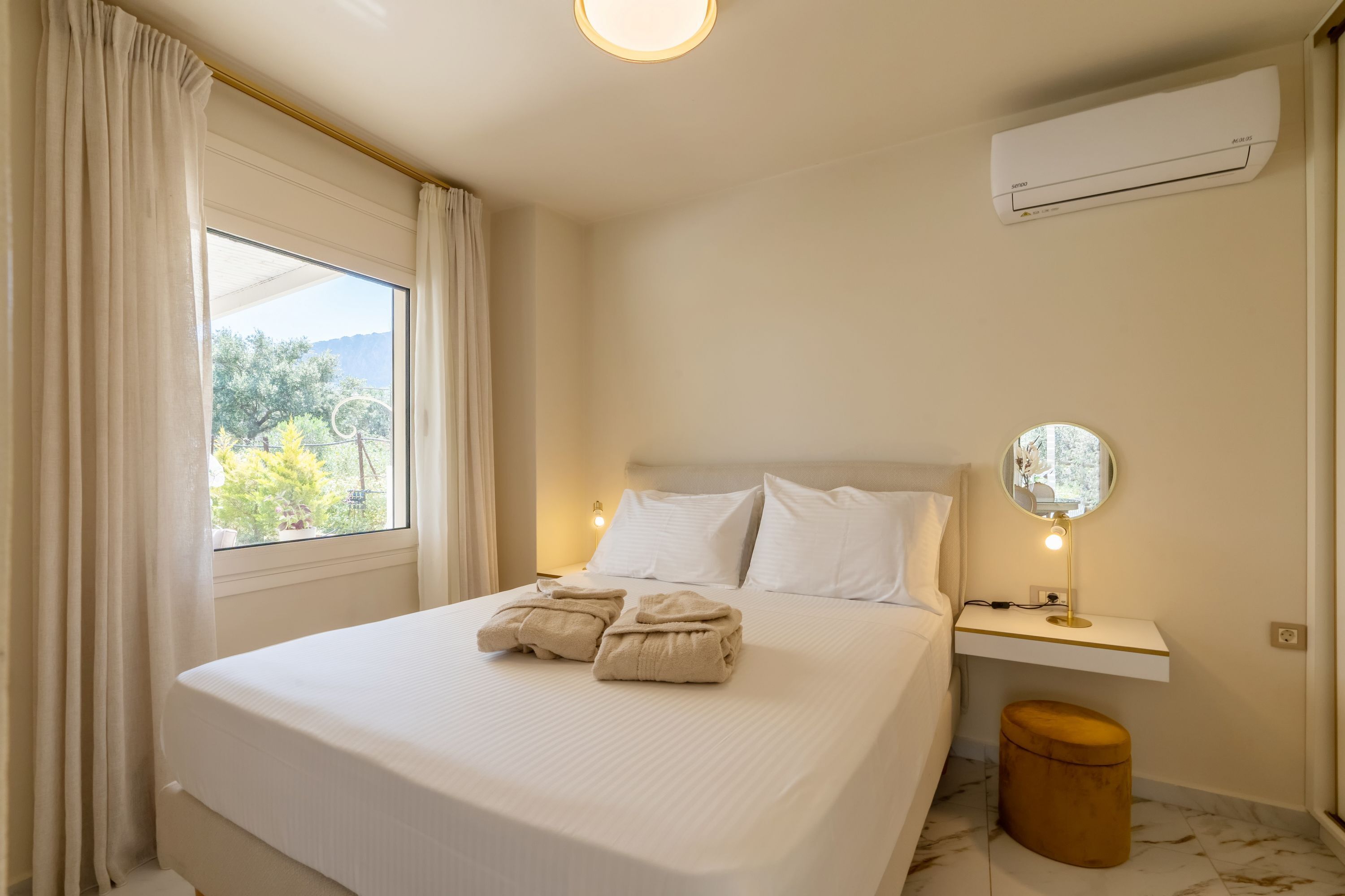 A hotel room with a bed, a bedside table with a lamp, a mirror, and an air conditioning unit.