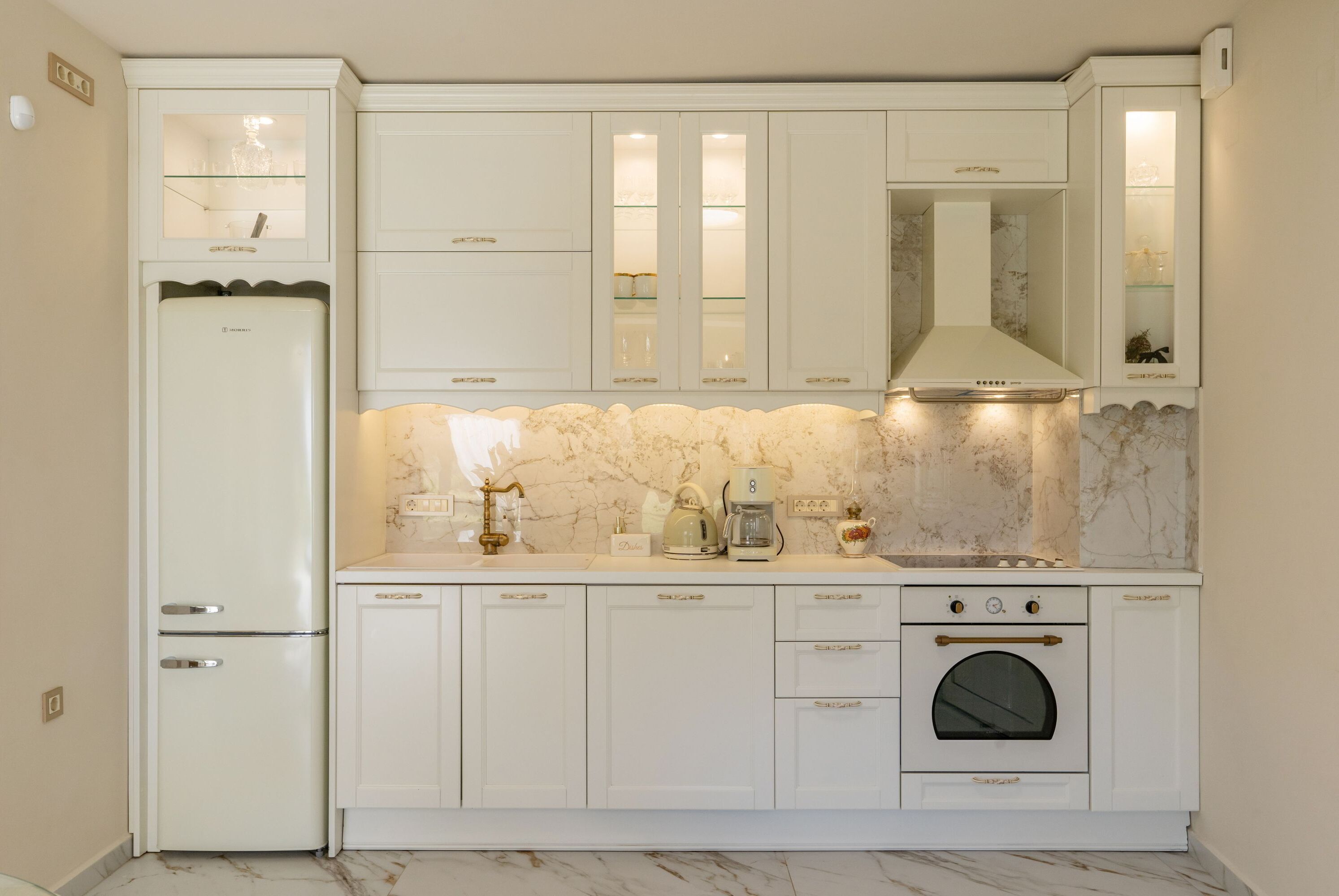 A kitchen with white cabinetry, a built-in oven, and a marble backsplash.