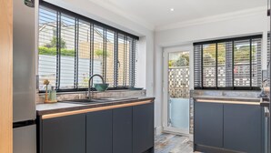 Une cuisine moderne avec des meubles de couleur sombre, un réfrigérateur en acier inoxydable et une fenêtre équipée de stores métalliques.