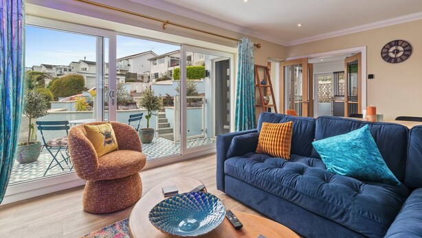 Un salon moderne avec un canapé bleu, un fauteuil au design original et à la texture particulière, une grande porte vitrée donnant sur un balcon et une table basse ronde.