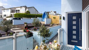 Une maison d’habitation avec une porte bleue, un mur blanc et un petit jardin fleuri.