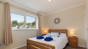 Quarto com cama de madeira, duas mesas de cabeceira com luminárias, uma janela com cortinas e um objeto decorativo na parede.