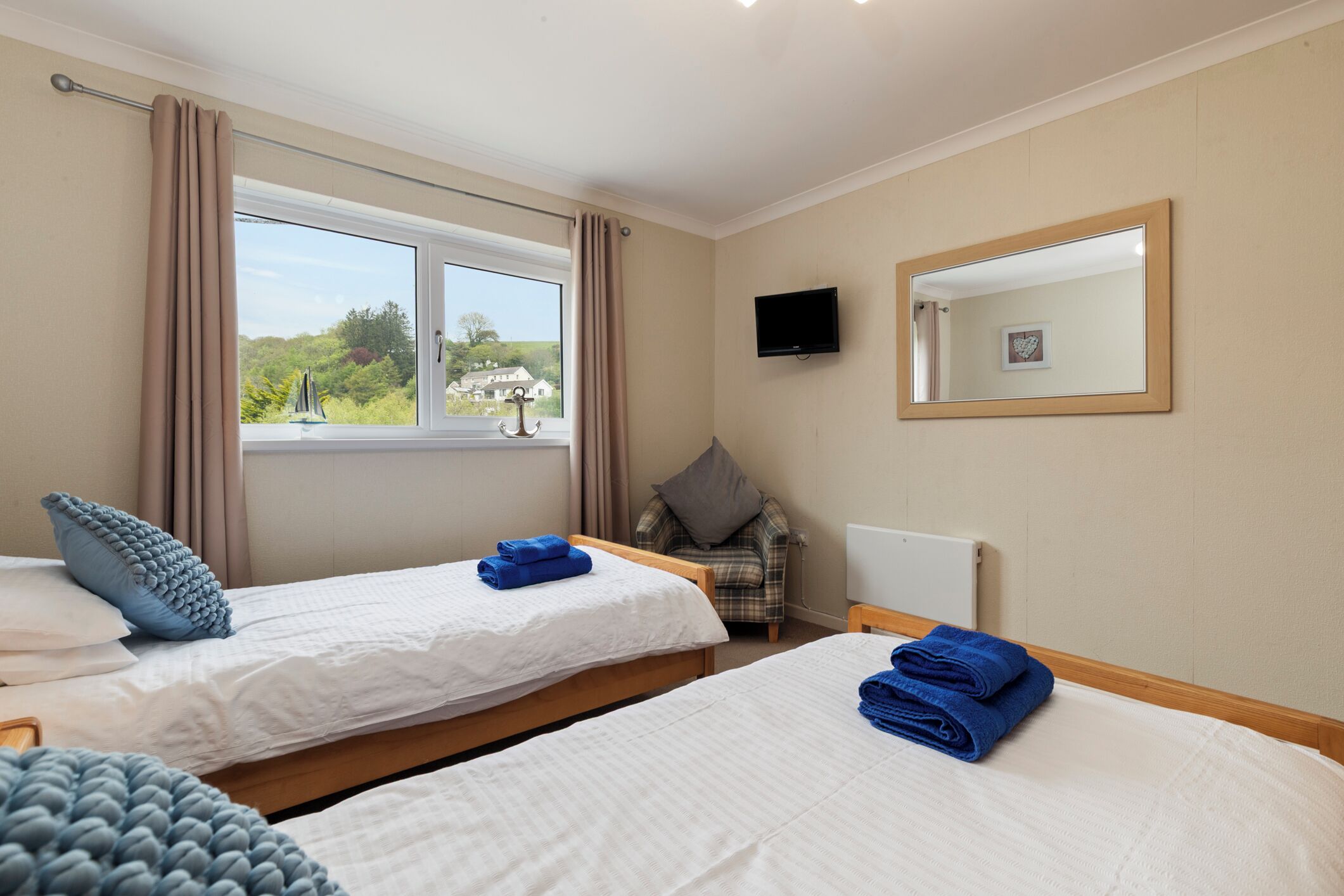 Une chambre d’hôtel avec deux lits, une chaise, une télévision et une fenêtre donnant sur un paysage agréable.