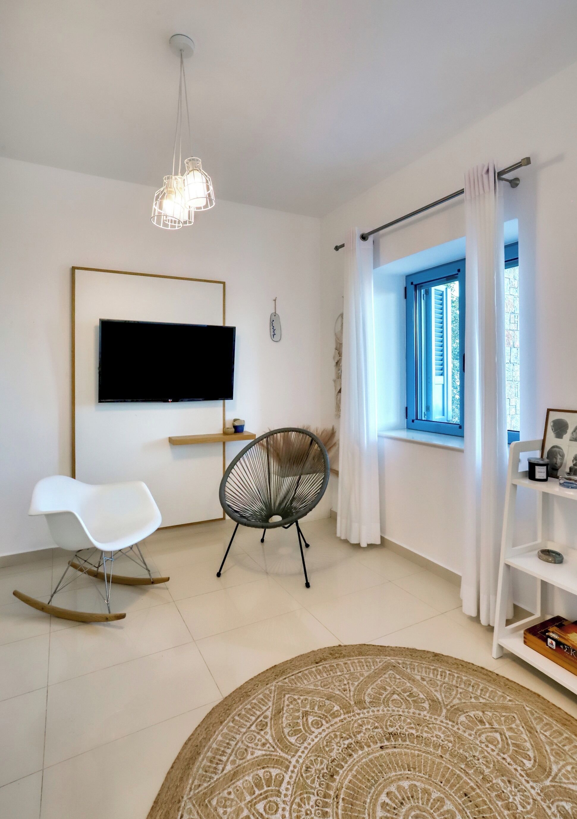 Un salon moderne avec un téléviseur à écran plat, un fauteuil à bascule, un fauteuil, un tapis à motifs et une fenêtre avec des rideaux.