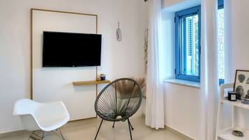 Un salon moderne avec un téléviseur à écran plat, un fauteuil à bascule, un fauteuil, un tapis à motifs et une fenêtre avec des rideaux.