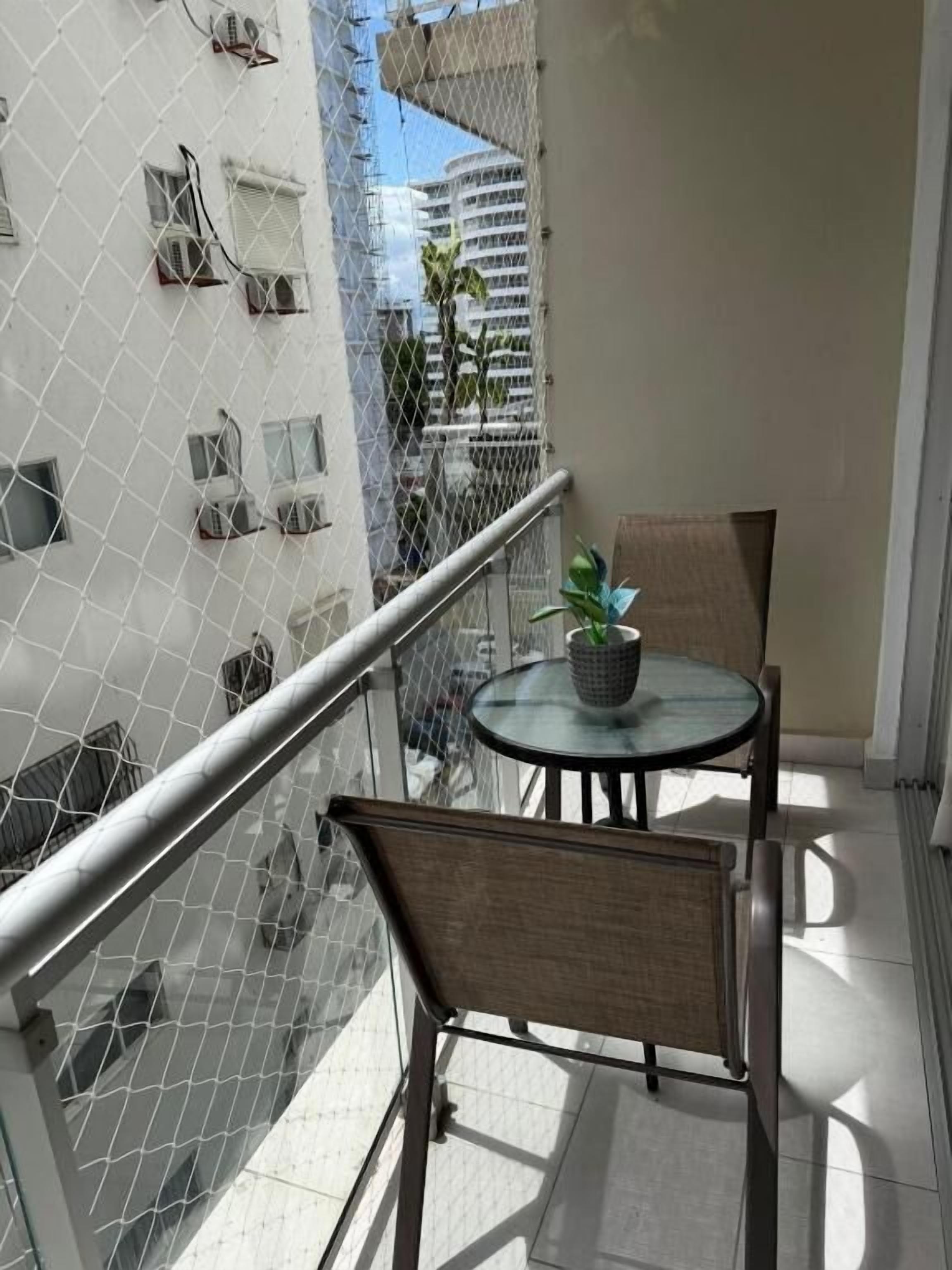 A balcony with a glass railing, a small round table, two chairs, and a potted plant.