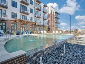 A swimming pool with lounge chairs and a building with multiple balconies in the background.