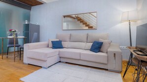 A modern living room with a sectional sofa, a dining table with chairs, a small kitchen area, and a staircase. - Exclusive loft in the center of Seville (Sevilla)