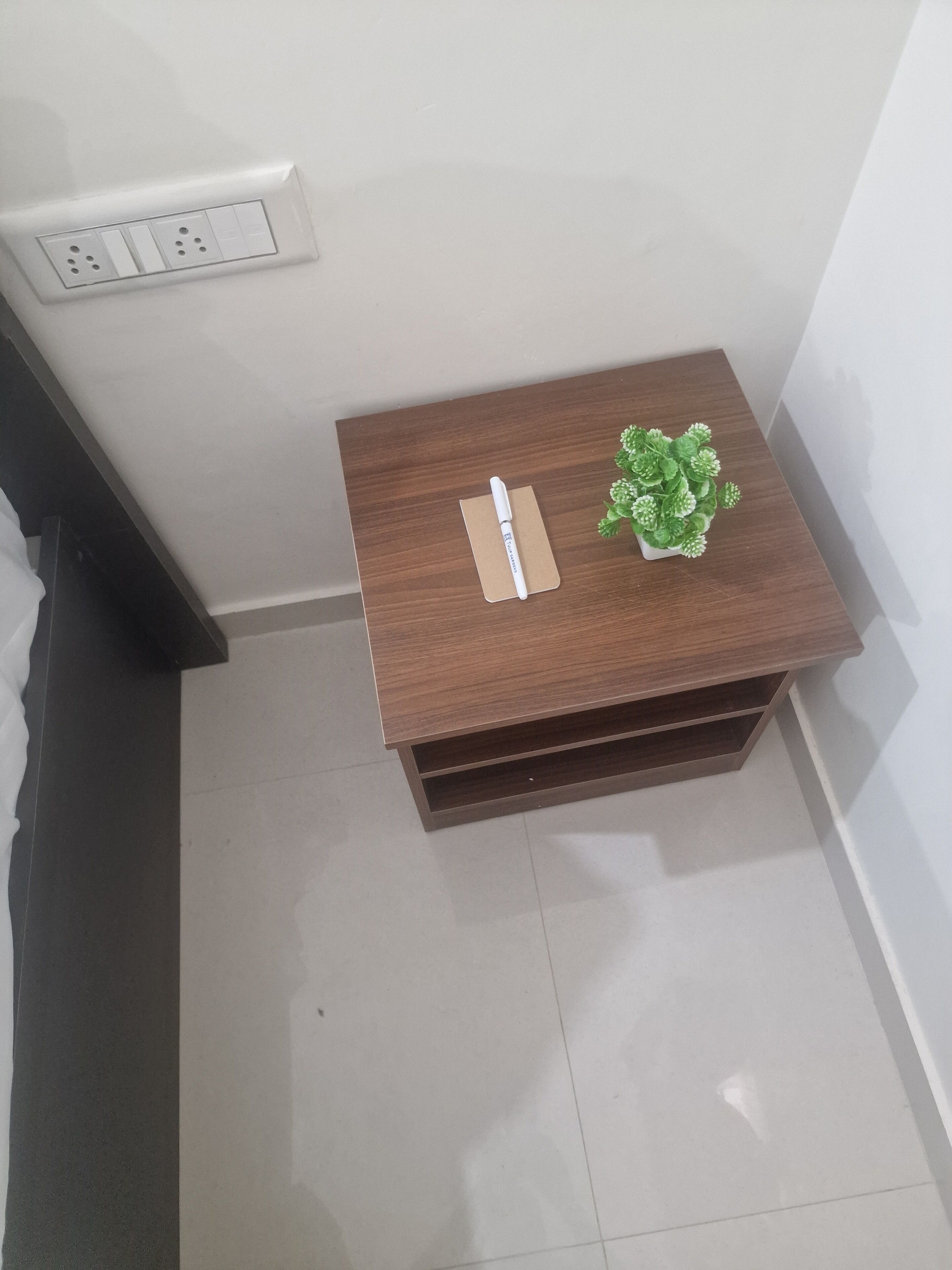 A small wooden side table with a white pen, a small potted plant, and a power outlet on the wall.