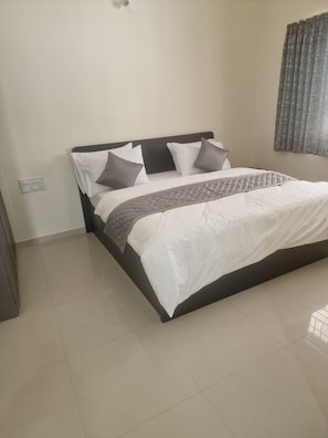 Una cama bien hecha con cabecera oscura, ropa de cama blanca y una manta acolchada gris.