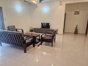 Una sala de estar con un sofá, dos sillones, una mesa de centro, un televisor, un aparador y una planta en maceta.