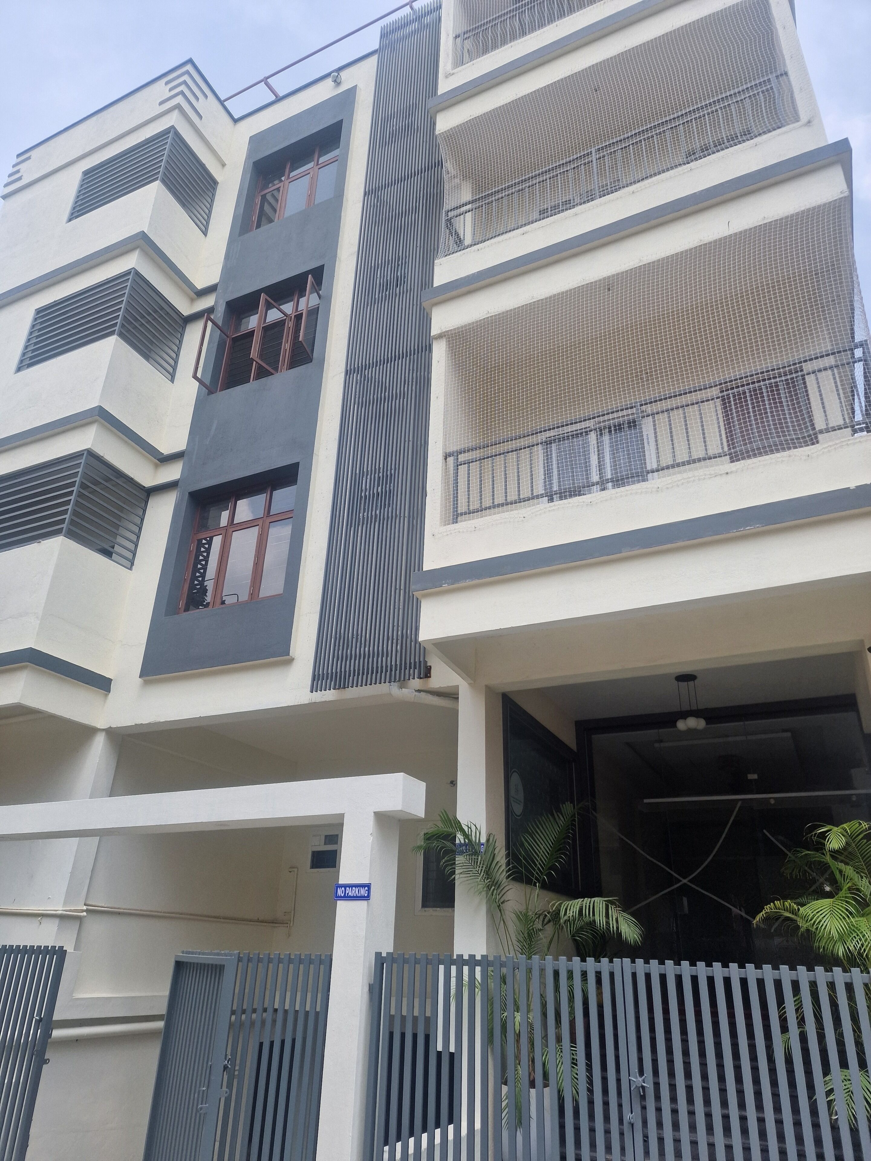A multi-story building with a 'NO PARKING' sign, a gated entrance, and a balcony with a railing.