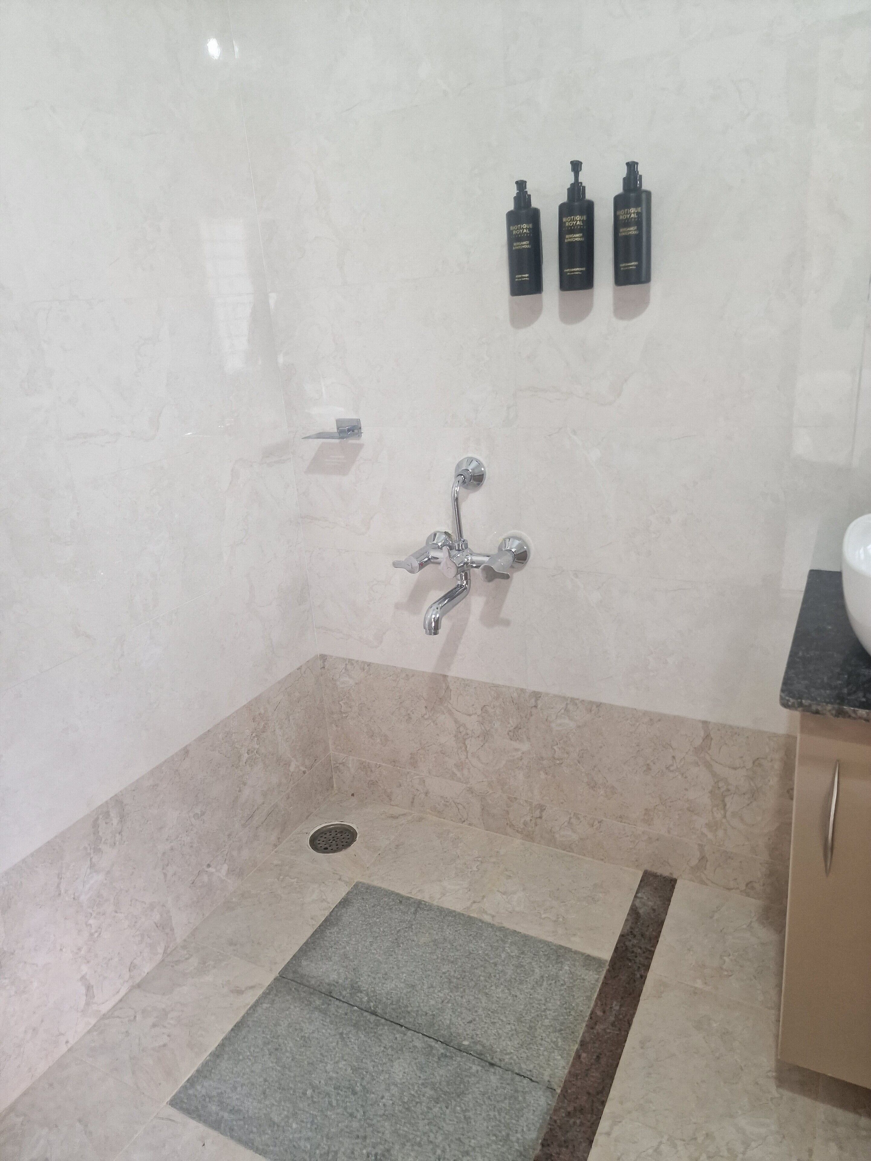 A bathroom with a shower, a sink, and three bottles of lotion on the wall.