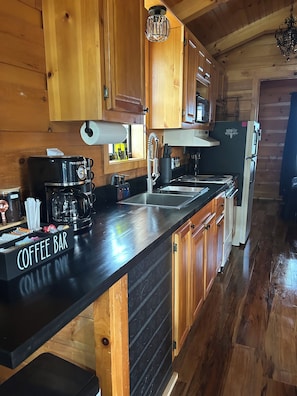 A kitchen with wooden cabinets, a coffee bar, a microwave, and a refrigerator. - Boulder Ridge Cabin 3: Romantic Lake Eufaula Cabin with Private Hot Tub (Checotah)