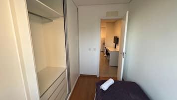 Een smalle gang met een bed, een kledingkast en een kitchenette achtergrond.