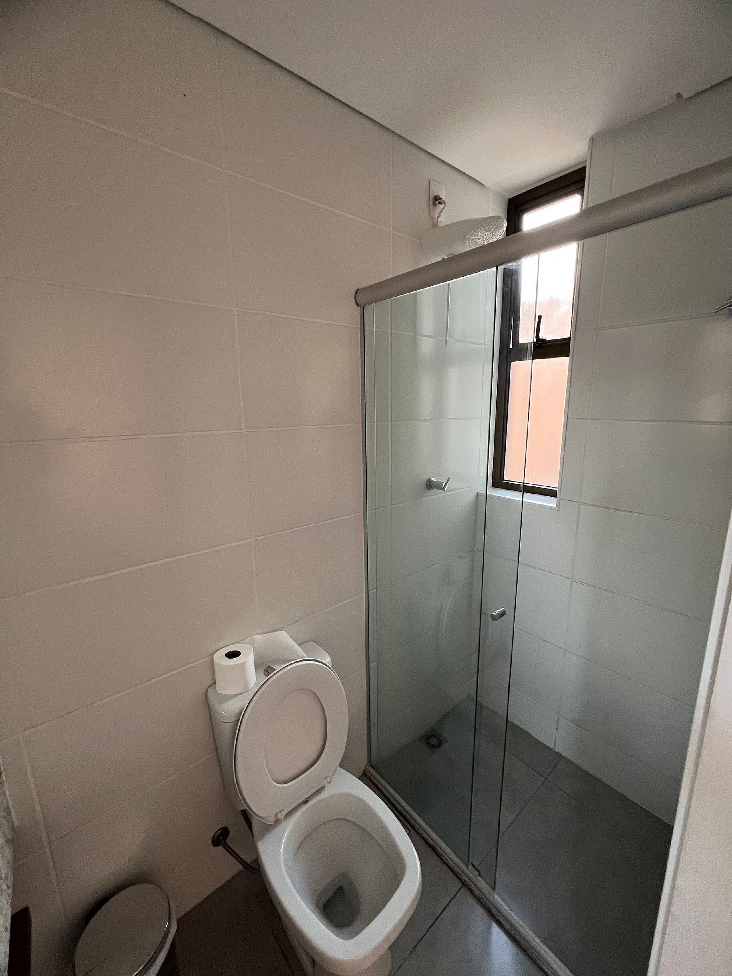 Ein Badezimmer mit Toilette, einer Duschkabine aus Glas und einem kleinen Fenster.